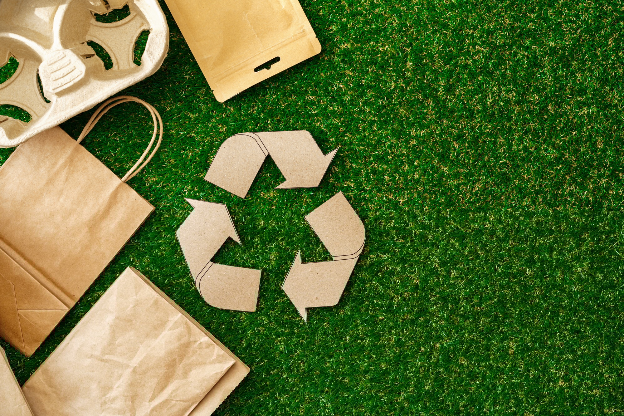 Recycling symbol surrounded by eco-friendly packaging on green grass background, representing sustainability and environmentally conscious equipment rental practices